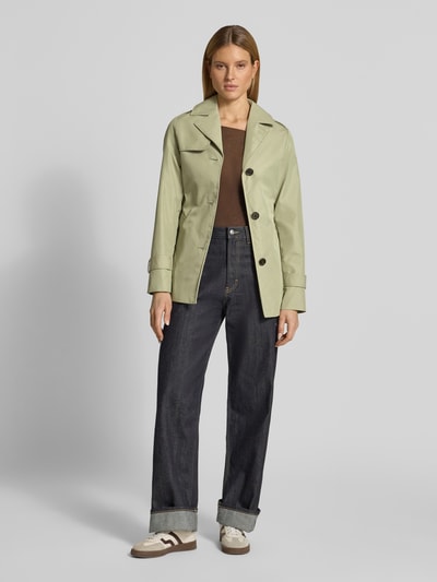Frauenmodel trägt Regular Fit Trenchcoat aus Baumwoll-Mix von s.Oliver RED LABEL in Hellgrün, unifarben, mit Reverskragen, Knopfleiste, Bindegürtel, langen Ärmeln, wasserabweisender Twill-Struktur; Ganzkörperansicht von vorne.
