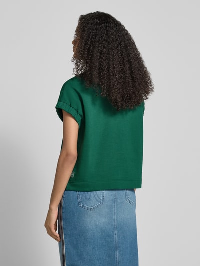 Frauenmodel trägt Relaxed Fit T-Shirt mit Logo-Detail von Marc Cain, grüner Baumwoll-Mix, teilelastische Ärmelabschlüsse, Rückansicht.