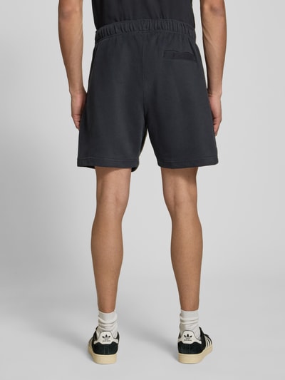 Männermodel trägt Shorts mit Logo-Stitching Modell 'ZANICA' von Ellesse aus Baumwoll-Mix in Schwarz, Relaxed-Fit, Ganzkörperansicht Rückansicht.