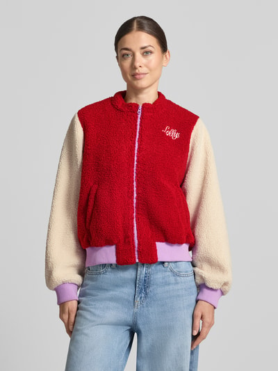 Frauenmodel trägt Fleecejacke mit label-Stickerei Modell 'Lua' von LOLLYS LAUNDRY in Rot und Beige, lockere Passform, Ganzkörperansicht von vorne.