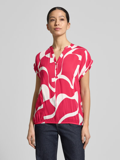 Frauenmodel trägt Regular Fit Bluse aus reiner Viskose Modell 'Miriama' von ZABAIONE in Pink mit weißem Muster, Kurzärmelig, Tunika-Ausschnitt, elastischer Bund, Rückenlänge bei Größe S: 62 cm, Ganzkörperansicht von vorne.