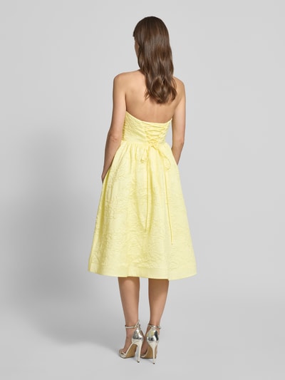 Frauenmodel trägt Minikleid mit floralem Allover-Stitching von Hey Kyla in Gelb, tailliert, schulterfrei, ausgestellte Form, Ganzkörperansicht Rückansicht.
