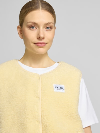 Frauenmodel trägt Regular Fit Weste in Teddy-Optik Modell 'AMALIA' von VILLA SOPHIE in Creme mit Druckknopfleiste, Nahaufnahme Oberkörper.