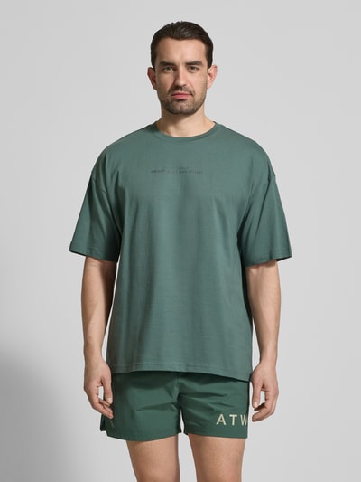 Männermodel trägt Boxy Fit T-Shirt mit Rundhalsausschnitt von HALO in Grün, Reine Baumwolle, überschnittene Schultern, Ganzkörperansicht von vorne.