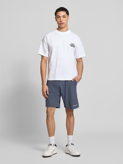 Männermodel trägt Shorts mit Logo-Print und Eingrifftaschen von ANOTHER COTTON LAB aus Baumwoll-Mix in Blau, Lockerer-Schnitt, Ganzkörperansicht von vorne.