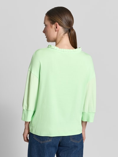 Vrouwenmodel draagt Longsleeve met tunnelkoord van Marc Cain in lichtgroen, los model, opstaande kraag met ruches, 3/4-mouw, elastische mouwboordjes, ruglengte bij maat 36: 57 cm. Ganzkörperansicht Rückansicht.