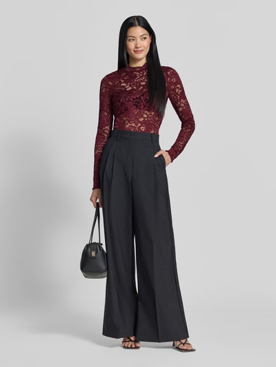 Frauenmodel trägt Slim Fit Longsleeve aus floraler Spitze Modell 'Lacey' von YAS in Bordeauxrot, semitransparentes Design, elastischer Material-Mix, kombiniert mit schwarzer weiter Hose, Ganzkörperansicht von vorne.