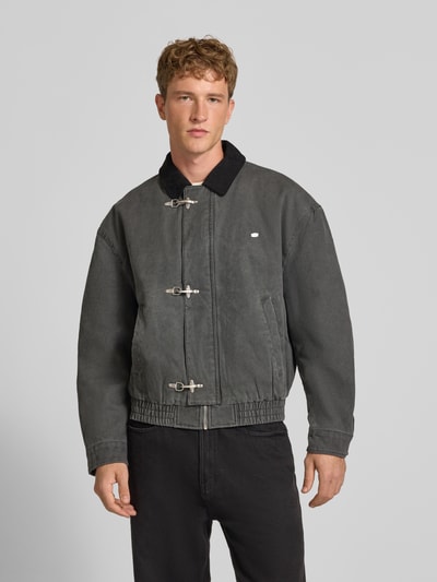 Männermodel trägt Gewaschene Bomberjacke mit Metallverschlüssen von REVIEW in Grau mit silbernen Verschlüssen, Regular Fit, Ganzkörperansicht von vorne. Reine Baumwolle, Eingrifftaschen, sichtbare Struktur der Stoffoberfläche. Rückenlänge M: 65 cm, Schulterbreite: 54 cm, Brustweite: 62 cm, Ärmellänge: 60 cm.