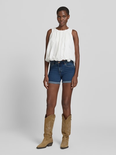 Frauenmodel trägt Regular Fit Jeansshorts aus Baumwoll-Mix Modell 'LUNA' von Vero Moda in Denim-Optik mit Label-Patch, 5-Pocket-Design, Knopf und verdecktem Reißverschluss, fixiertem Umschlag, Ganzkörperansicht von vorne.