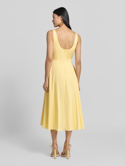 Frauenmodel trägt Midikleid mit Rundhalsausschnitt Modell 'NICOLE' von MANGO aus gelbem Baumwoll-Elasthan-Mix, taillierter Schnitt, Ganzkörperansicht Rückansicht.