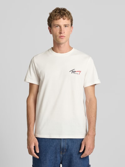 Männermodel trägt Slim Fit T-Shirt aus reiner Baumwolle von Tommy Jeans in Offwhite mit Logo, glatte Textur, Ganzkörperansicht von vorne.