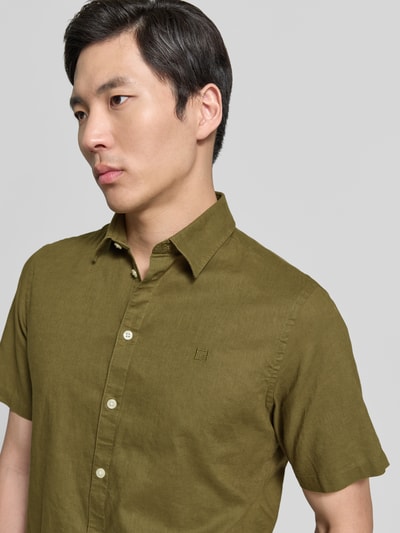 Männermodel trägt Slim Fit Freizeithemd aus Leinen-Baumwoll-Mix Modell 'AKSEL' von Casual Friday in Olive mit Knopfleiste, Label-Stitching, Kentkragen, Nahaufnahme Oberkörper. Rückenlänge bei Größe M: 78 cm, Schulterbreite: 45 cm, Ärmellänge: 27 cm.