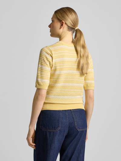 Vrouwenmodel draagt gebreide pullover uit katoenmix van Scotch & Soda in geel met tricotlook, getailleerde pasvorm, ronde hals, 3/4-mouw, ruglengte maat S 52 cm, mouwlengte maat S 30 cm. Ganzkörperansicht Rückansicht.