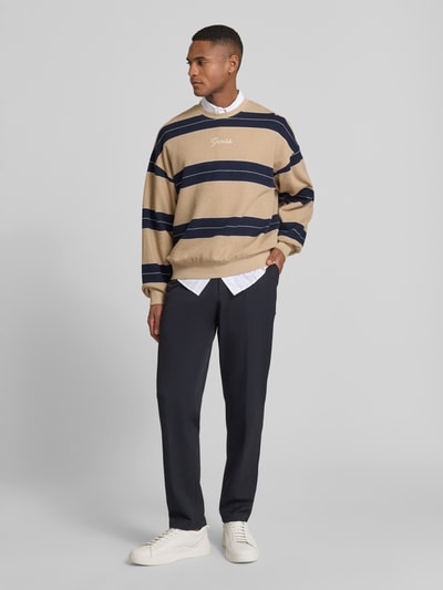 Männermodel trägt Guess Sweatshirt mit Label-Stitching aus katoen, los model, geribde boorden, ronde hals, beige en marineblauw, Ganzkörperansicht von vorne.