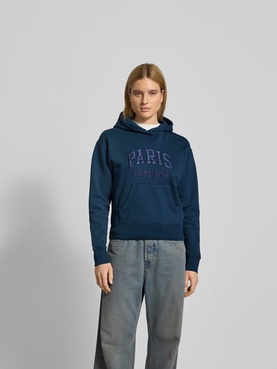 Frauenmodel trägt Regular Fit Hoodie mit Logo-Stitching von Anine Bing in Dunkelblau, Reine Baumwolle, Känguru-Tasche, Elastische Abschlüsse, Rückenlänge bei Größe S 58 cm, Ganzkörperansicht von vorne.