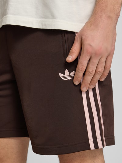 Männermodel trägt Regular Fit Sport-Shorts mit Kontraststreifen Modell 'FIREBIRD' von adidas Originals, Nahaufnahme Oberschenkel, Optik: Unifarben, Passform: Regular-Fit, Logo-Stitching, Details: Kontraststreifen, Verschluss: Tunnelzug innen, Bundabschluss: elastisch, Taschen: seitliche Reißverschlusstasche.
