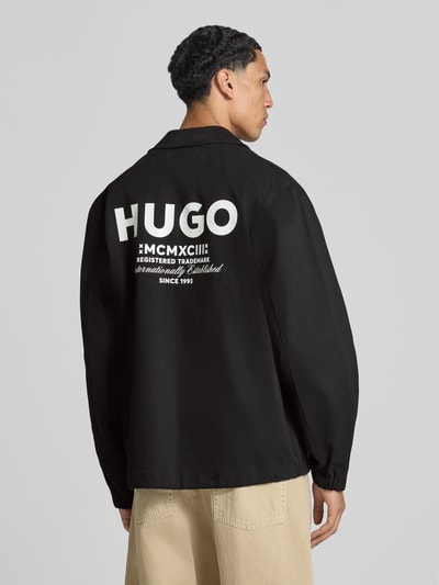 Männermodel trägt schwarze Regular Fit Bomberjacke / Blouson aus reiner Baumwolle Modell 'Biyo2631' von HUGO, Herren Bomberjacke, Ganzkörperansicht Rückansicht.
