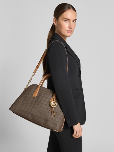 Kobiece modelka nosi torebkę Handtasche mit Logo-Muster Modell 'FREDDIE' od MICHAEL Michael Kors, brązowy wzór z logo, złota aplikacja z logo, uchwyty i pasek na ramię, Główna przegroda z zamkiem błyskawicznym, Szerokość w rozmiarze 1: 40 cm, Długość w rozmiarze 1: 28 cm, Głębokość w rozmiarze 1: 15 cm, długość paska na ramię: 102 cm, Ganzkörperansicht z przodu.