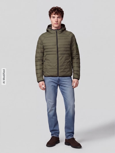 Mężczyzna model nosi oliwkową kurtkę pikowaną z kapturem Regular Fit Steppjacke mit Kapuze Modell 'OW_Urbanex' od BOSS Green, jeansy i ciemne buty, jednolite tło, widok całej sylwetki od przodu, zdjęcie KI-modifiziertes Bild.