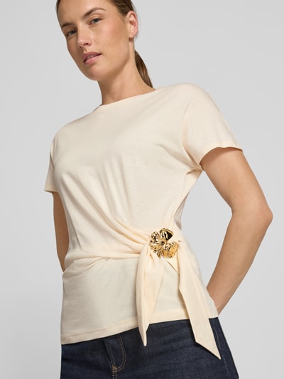 Frauenmodel trägt T-Shirt in Wickel-Optik mit Brosche von Christian Berg Woman Selection aus reiner Baumwolle in Creme, Nahaufnahme Oberkörper.