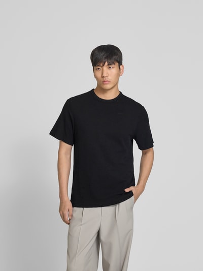Männermodel trägt Relaxed Fit T-Shirt mit Strukturmuster von Forét in Schwarz aus Reine Baumwolle mit Logo-Stitching, Rundhalsausschnitt, Rückenlänge 69 cm bei Größe M, Ganzkörperansicht von vorne.