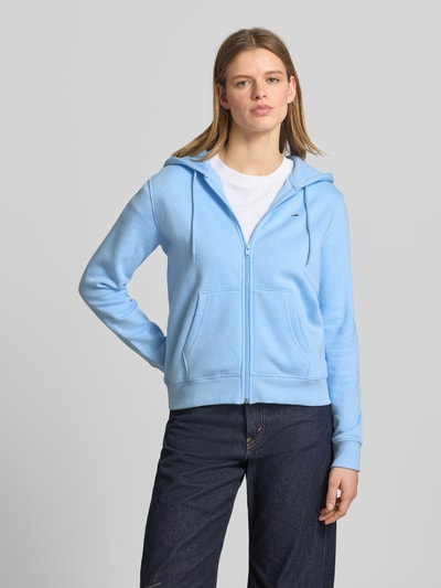 Frauenmodel trägt Regular Fit Sweatjacke aus Baumwoll-Mix von Tommy Jeans in Hellblau, Kapuze, Kängurutasche, Sweatstoff, Ganzkörperansicht von vorne.