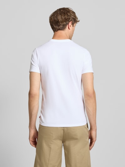 Männermodel trägt weißes Slim Fit T-Shirt aus reiner Baumwolle Modell '2PK CREWNECK GRAPHIC' von Levi's® zu beigefarbener Hose, Herren T-Shirt-Set von Levi's®, Ganzkörperansicht Rückansicht.