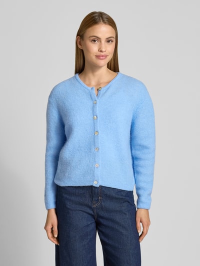 Frauenmodel trägt Strickjacke mit Knopfleiste Modell 'VITOW' von American Vintage in Hellblau, lockerer Schnitt, Rundhalsausschnitt, gerippte Abschlüsse, Alpaka-Lanawoll-Mix mit Stretch-Anteil, Ganzkörperansicht von vorne.