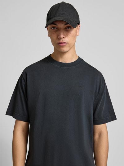 Männermodel trägt Regular Fit T-Shirt aus reiner Baumwolle von Closed in dunklem Used-Look mit Label-Print, Nahaufnahme Oberkörper.