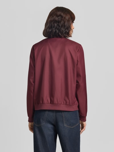 Frauenmodel trägt Bomberjacke mit Eingrifftaschen Modell 'PAPAYA' von VILA in dunklem Rot, glatte Textur, Jeans kombiniert, Ganzkörperansicht Rückansicht. Regular Fit, Stehkragen, Reißverschluss, Rückenlänge 49 cm, Schulterbreite 35 cm, Brustweite 52 cm, Ärmellänge 62 cm.