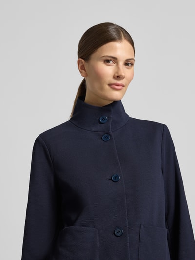 Modelka kobieca nosi Regular Fit Jacke mit Stehkragen od WHITE LABEL, elastyczna mieszanka bawełny, krój regular fit, stójka, naszyte kieszenie, pełny rząd guzików, długość tyłu w rozmiarze 36: 57 cm, szerokość w rozmiarze 36: 50 cm, długość rękawa w rozmiarze 36: 65 cm, granatowa tkanina o delikatnej strukturze, widok na górną część ciała z przodu