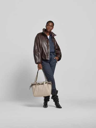 Frauenmodel trägt Bucket-Bag mit Drawstring-Verschluss von Tory Burch mit Strukturmuster, Innenfach und langem Trageriemen, Ganzkörperansicht von vorne.