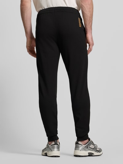 Männermodel trägt Sweatpants mit Logo und elastischem Bund von EA7 Emporio Armani, Schwarz, Regular Fit, Ganzkörperansicht Rückansicht.
