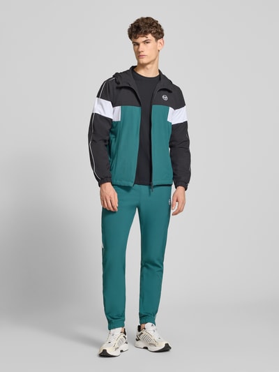 Męski model nosi Sweatpants mit Logo-Stitching Modell 'CASPIO' od SERGIO TACCHINI, materiał z domieszką stretchu, elastyczny pas ze sznurkiem, kieszenie boczne, krój slim fit, ściągacze, kolor zielony, długość nogawki wewnętrznej w rozmiarze M: 78 cm, widok całej sylwetki z przodu