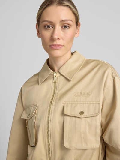 Vrouwenmodel draagt Jacke met Cargotaschen model 'JULIANE' van GUESS in beige katoenmix met labelstitching, regular fit, platte kraag, ritssluiting, elastische band, detailopname bovenlichaam.