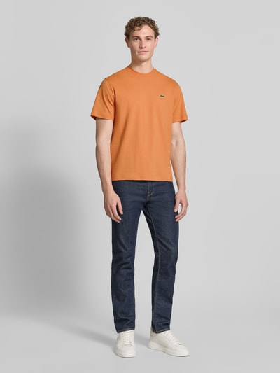 Mannenmodel draagt Regular Fit poloshirt uit puur katoen van Lacoste, look: effen, regular fit, logostitching, ronde hals, korte mouw, materiaal: puur katoen, effen oranje, detail met logo-applicatie, voorkant, geheellichaamsbeeld.
