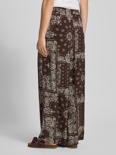 Frauenmodel trägt Relaxed Fit Weite Hose aus reiner Viskose Modell 'KAVI' von Only in Braun mit hellem Paisley-Muster, Damen Weite Hose, Ganzkörperansicht Rückansicht.
