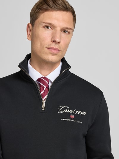 Männermodel trägt Sweatshirt mit Stehkragen und Reißverschluss von Gant, Logo-Stickerei, schwarz, Baumwoll-Mix, Nahaufnahme Oberkörper.