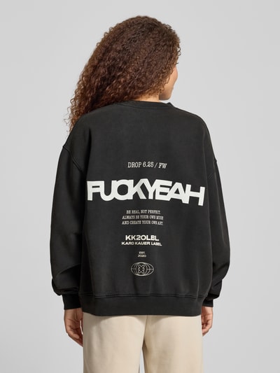 Frauenmodel trägt Oversized Sweatshirt mit Statement-Print von Karo Kauer in Schwarz mit weißen Akzenten, reine Baumwolle, gerippte Abschlüsse, Rundhalsausschnitt, Ganzkörperansicht Rückansicht.