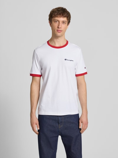 Männermodel trägt T-Shirt mit Rundhalsausschnitt und Label-Stitchings von CHAMPION in Weiß mit roten Akzenten, Reine Baumwolle, Regular-Fit, Rückenlänge bei Größe M: 70 cm, Ganzkörperansicht von vorne.
