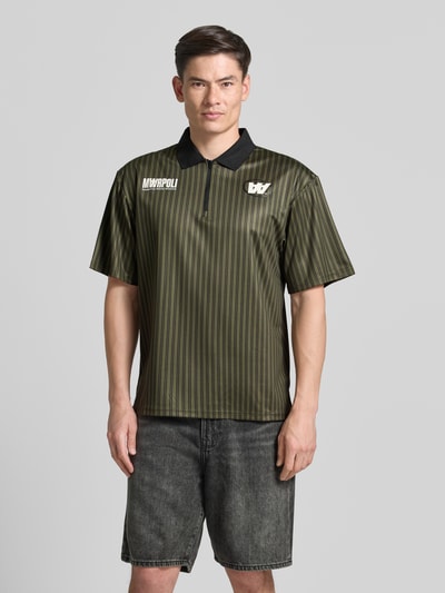 Męski model nosi koszulkę polo Regular Fit Poloshirt mit Label-Print model 'Lama' od Wood Wood w paski, kołnierzyk polo, krótki zamek błyskawiczny, nadruk z logo, długość tyłu w rozmiarze M: 72 cm, pełny przód