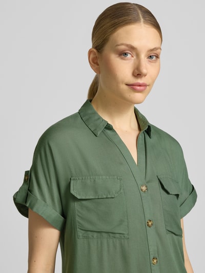Modelka kobieca nosi Regular Fit Hemdbluse aus reiner Viskose Modell 'BUMPY' od Vero Moda, zielona, gładka, krój regular fit, dekolt V, krótkie rękawy z mankietem, naszywane kieszenie, widok z przodu, zbliżenie na górną część sylwetki.