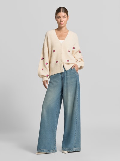 Vrouwenmodel draagt cardigan met overslagen schouders Model 'FLEUR' van YAS, materiaalmix met katoen, loose fit, V-hals, knoopsluiting, ruglengte 52 cm, mouwlengte 52 cm, bloemenmotief in crème, lila en roze tinten, grof gebreide textuur, geheel vooraanzicht