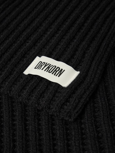 Produktfoto, schwarzer Grobstrick Schal mit weißem Label-Detail, Modell 'NUMAS' von DRYKORN, Material-Mix mit Alpaka-Anteil, Detailaufnahme