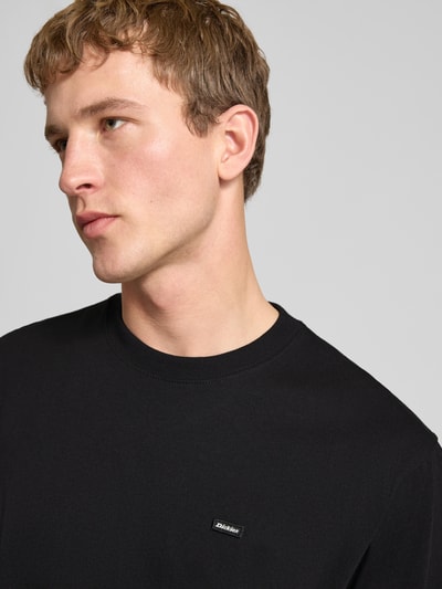 Männermodel trägt T-Shirt mit Label-Detail und Rundhalsausschnitt von Dickies in Schwarz, aus Baumwolle, Relaxed Fit, Nahaufnahme Oberkörper.