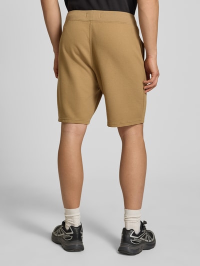 Mannelijk model draagt Straight Fit Shorts met structuurpatroon van G-Star Raw, elastische materiaalmix met katoen, logodetail, elastische band, kleur beige, ganzkörperansicht rückansicht.