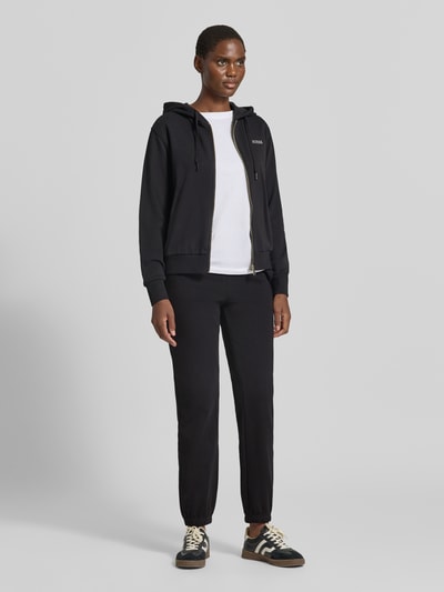 Vrouwenmodel draagt zwarte sweatjack met capuchon van katoenmix, regular fit, Model 'SOFIA' van GUESS, labelstitching, ritssluiting, geheel aanzicht van voren.