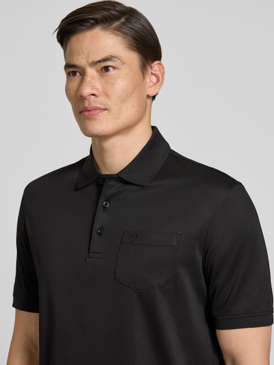 Männermodel trägt Regular Fit Poloshirt mit Brusttasche und Label-Stitching von bugatti in Schwarz, feine Textur, Nahaufnahme Oberkörper.
