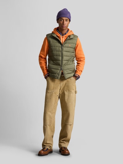 Männermodel trägt Regular Fit Weste mit Logo-Stitching von Polo Ralph Lauren in Grün auf orangefarbenem Hoodie, Ganzkörperansicht von vorne.