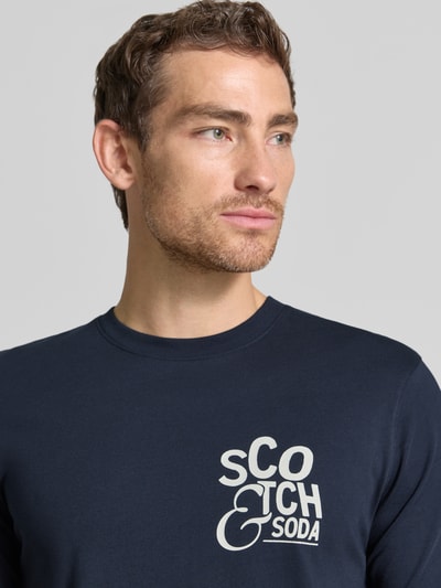Męski model nosi Regular Fit T-Shirt mit Logo-Print von Scotch & Soda, granatowy kolor, bawełna, okrągły dekolt, Nahaufnahme górnej części ciała, długość tyłu w rozmiarze M: 73 cm.